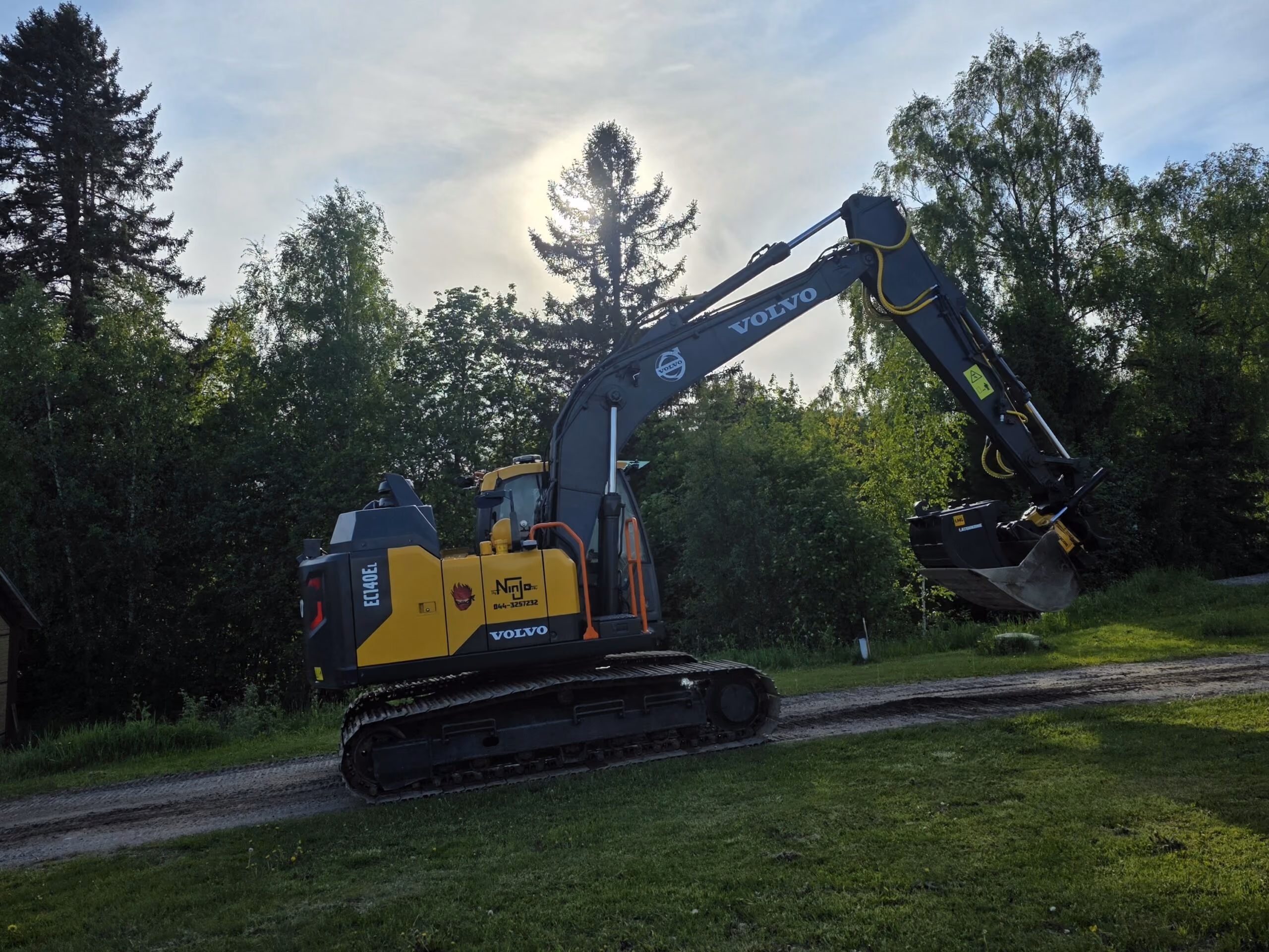 Volvo EC140EL i Oy NinJo Ab:s färger på en grusväg i kvällsljus